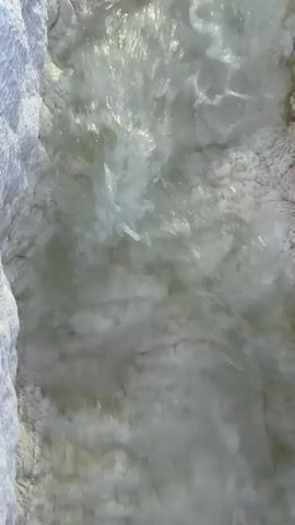 A stream of water flows between white, textured rock formations. The water is clear and turbulent, reflecting light as it rushes by.