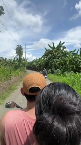 Moped riders travel dirt road through banana trees in Carmen