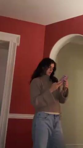 A person stands in a corner between a doorway with red walls and an arched doorway with yellow walls. The person holds a phone, looks at it, and then lifts the phone toward the arched doorway to seemingly take a picture or video of it.