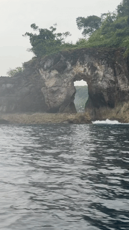 Boat approaches natural sea arch near Nusa Penida, Indonesia