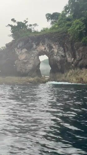 Boat approaches natural sea arch near Nusa Penida, Indonesia