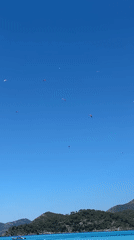 Paragliders soar above busy Fethiye beach on sunny morning
