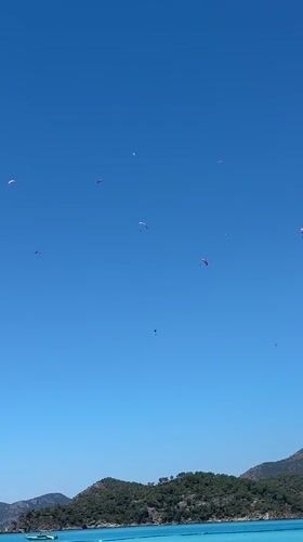Paragliders soar above busy Fethiye beach on sunny morning