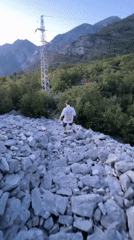 Person walks rocky slope toward ocean view in Šušanj