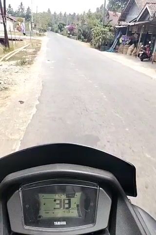 This is a first-person perspective video of someone riding a Yamaha motorcycle down a paved road. The rider's view is focused on the dashboard, which displays the speed increasing from 39 km/h to 43 km/h. The road appears to be in a rural or suburban area with trees and buildings visible on the sides. The time appears to be daytime.