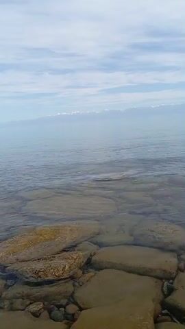 The video shows a body of water with rocks at the bottom. The water is clear enough to see the rocks. The sky is cloudy and the horizon is visible in the distance. There are no people or animals in the video. The scene appears to be a natural environment.