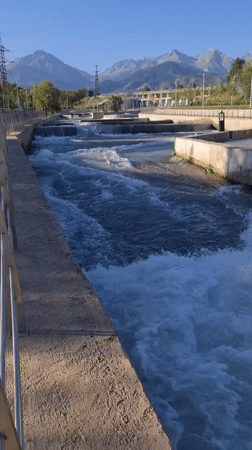 Turbulent water churns through a concrete river channel in Almaty