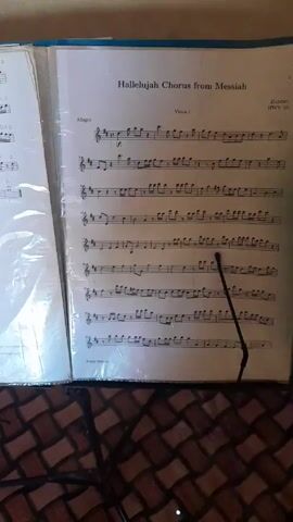 Here's a description of the video:

The video shows a music stand with sheet music open to a page titled "Hallelujah Chorus from Messiah." A person's hand holding a green cleaning brush is moving it back and forth in front of the sheet music. The background is a checkered floor.