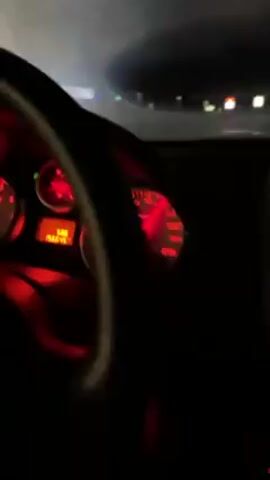 The video shows the interior of a car driving at night. The dashboard is illuminated in red light, displaying the speedometer reading over 160 km/h and the odometer showing 156645. A glimpse of the tachometer on the left and another small gauge in the center are also visible. The driver is operating the vehicle on a highway, which is visible through the windshield. Other cars are present on the road, marked by their headlights and taillights. The overall environment is dark, with only the artificial lights of the car and other vehicles illuminating the scene.