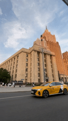 Yellow taxi passes ornate Moscow building as pedestrians walk nearby