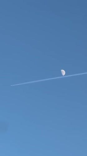 Jet contrail crosses moon over The Hague evening sky