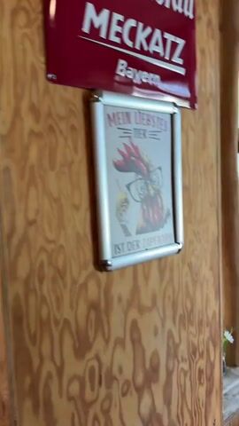 The video pans across the interior of a rustic restaurant. Wooden walls and ceilings are prominent. On the left wall, a skull is mounted. Further into the restaurant, tables with white tablecloths and booths are visible. One table has flowers and salt and pepper shakers. Another booth has red cushions. In the background, a counter area is visible with various items on display, including flowers and what appears to be barware. The lighting is warm, and the overall ambiance suggests a cozy and traditional dining establishment.