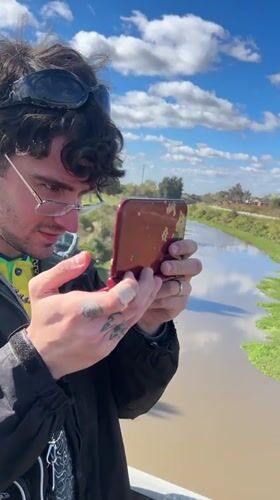 Man plays Nintendo 3DS on bridge overlooking canal