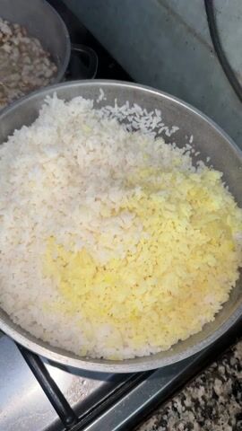 Here's a detailed description of the video:

The video shows a stovetop with several pots and pans. In the foreground, a large pot contains a mix of white and yellow rice. Someone stirs the rice with a spoon. To the left, a pot of cooked beans is also being stirred. Behind these are a pan with a red sauce and another pan with fried food, possibly chicken. The stovetop is stainless steel with black accents. The overall environment appears to be a kitchen.