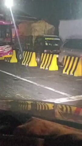 The video shows a nighttime traffic jam on a highway. Several large buses and trucks are stopped on the road. Yellow and black traffic barriers are placed in front of some of the vehicles. The headlights of the vehicles are on, illuminating the scene. The camera appears to be inside another vehicle, looking out. The overall impression is of a significant traffic blockage.