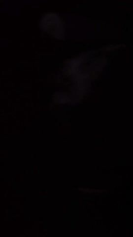 A person's mouth is barely visible in an otherwise pitch-black scene. The mouth opens and closes abruptly before the scene returns to darkness.