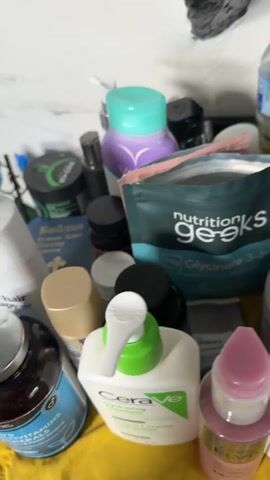 The video shows a close-up view of a cluttered surface, likely a vanity or shelf, filled with various personal care products, cosmetics, and accessories. The items are densely packed, creating a chaotic and colorful display. Among the visible items are bottles of various sizes and shapes, tubes, jars, a comb, and a small mirror. Some of the products appear to be skincare, haircare, and potentially makeup. The lighting suggests an indoor environment, and the focus is on the assortment of items rather than a specific action or person. The overall impression is one of a well-used collection of beauty and personal hygiene products.