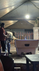 Two men play pool on covered patio in Ado