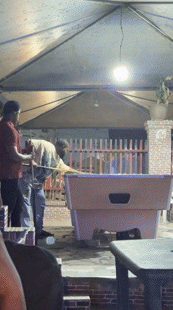 Two men play pool on covered patio in Ado