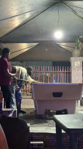 Two men play pool on covered patio in Ado