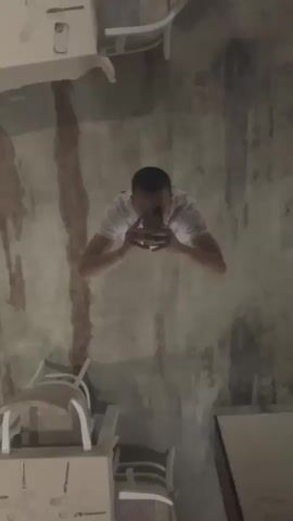 The media file is a video showcasing a dining room with a long, elegantly set table. The camera appears to be positioned close to the floor, possibly on a rolling object, as it moves through the space. The initial frames show a reflection in what looks like a mirror or a highly polished surface, with a person holding a phone, taking the initial shot. This reflection is upside down and somewhat distorted.

As the camera moves, the scene shifts to reveal a long banquet table, covered with a neutral-colored tablecloth. The table is set for a formal meal, with multiple place settings, each featuring glasses, silverware, and napkins. Several chairs are positioned around the table, upholstered in a light-colored fabric with white wooden frames. The room's decor includes textured walls with vertical wooden slats and elegantly draped curtains. There are also visible ceiling fixtures, including lights and ventilation systems.

The overall impression is that of a well-appointed dining area, possibly in a restaurant, hotel, or event venue. The lighting suggests it could be evening or an indoor setting with artificial lighting. There are no specific details about the time of day, weather, or emotions conveyed by the scene, as it focuses on the setting itself. No visible text is present in the video. The location context provided, Mineralni Bani, Bulgaria, suggests this is likely a dining establishment in that region. The initial distorted reflection adds a touch of artistic or unconventional perspective to the beginning of the video.