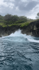 Boat passengers film dramatic Nusa Penida coastline and clifftop statue