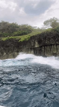 Boat passengers film dramatic Nusa Penida coastline and clifftop statue