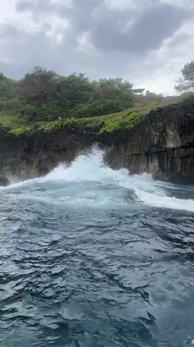 Boat passengers film dramatic Nusa Penida coastline and clifftop statue