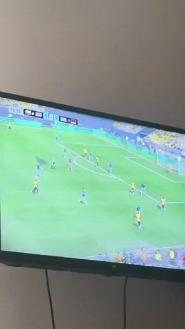 This video captures a television screen displaying a soccer match. The score is 1-1, and the time is 19:58. The game appears to be played on a bright green field with white lines. Several players are visible on the field, some wearing yellow and blue uniforms, while others are in teal uniforms. The scoreboard at the top of the screen shows team names and flags. The overall environment appears to be a dimly lit room, with the television screen being the primary light source.