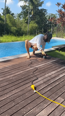 Worker sands wooden pool deck in Ubud, Indonesia