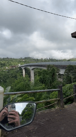 Motorcycle crosses bridge over green valley in Petang, Indonesia