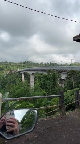 Motorcycle crosses bridge over green valley in Petang, Indonesia