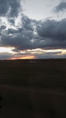 Sunset breaks through storm clouds over field, captured from vehicle