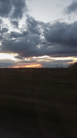 Sunset breaks through storm clouds over field, captured from vehicle