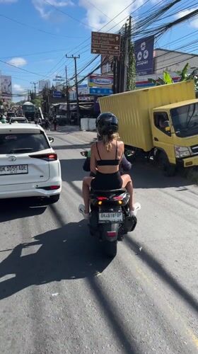 Two passengers on scooter travel alongside white car in Ungasan