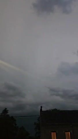 The video shows a building with lights on in its windows, set against a backdrop of a stormy sky. A flash of lightning illuminates the sky and then disappears, leaving behind a gray, cloudy atmosphere. The scene appears to be at dusk or during a storm.