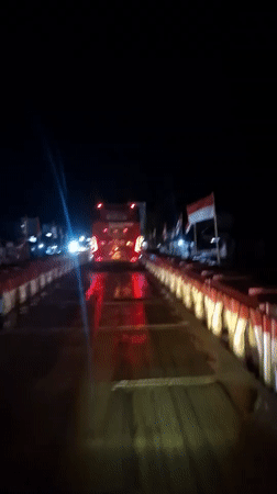 Nighttime bridge crossing with illuminated red bus captured in Indonesia