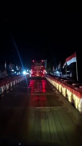 Nighttime bridge crossing with illuminated red bus captured in Indonesia