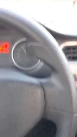 A car's perspective on a highway shows two Mercedes cars ahead. The lead Mercedes is black, and the trailing one is gray. A truck is further ahead in the same lane as the Mercedes vehicles. The camera's angle shows the steering wheel, dashboard, and a partial view of the driver in the rearview mirror. The sunset is visible in the rearview mirror. The car travels under a concrete overpass.