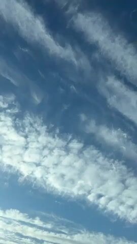 The video shows a shot of the sky. The sky is blue with white clouds. The clouds form both flat streaks and fluffy patches.