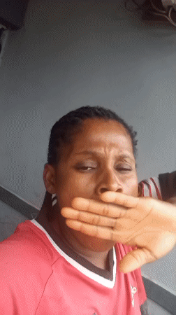 Hand raised to mouth, leaning against a gray wall outside
