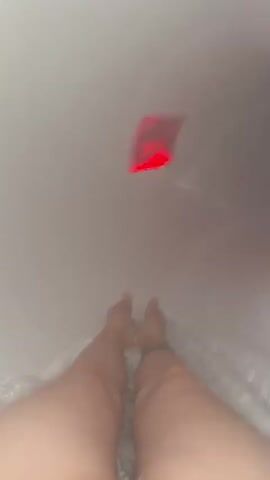 The video shows a person sitting at the top of a water slide, with their feet visible in the foreground. The camera then slides down the slide, which is illuminated with red, blue, and purple lights. The person yells as they descend. The viewpoint of the camera is first-person and follows the person down the slide.