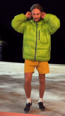 Man in green jacket jumps with raised arms outdoors