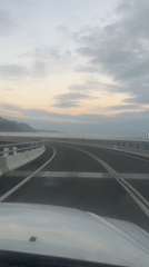 Car travels coastal highway at dawn with overcast skies