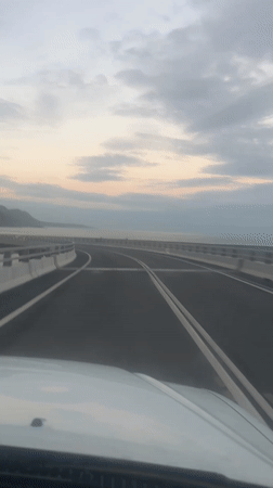Car travels coastal highway at dawn with overcast skies