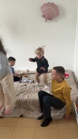 The video shows children in a room, jumping and playing on a bed. There's a baby lying on the bed as well. A woman dressed as Ariel from "The Little Mermaid" is shown with a group of children, interacting with them. The room is decorated with balloons and a seashell decoration. The setting appears to be a birthday party or a similar event.