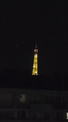 This is a video of the Eiffel Tower at night. The iconic landmark is lit up in a bright yellow, its structure clearly visible against the dark sky. The tower appears to be twinkling, suggesting it might be sparkling or illuminated with many lights. Below the tower, the silhouette of a building is visible, with some windows showing faint light. The overall scene conveys the grandeur of the Eiffel Tower, especially when illuminated at night. The time of day is clearly night, and there are no visible indications of weather. The location is identified as Montrouge, France, which is a commune in the southern suburbs of Paris. The video does not contain any visible text. The overall mood is one of awe and wonder, capturing the magic of Paris at night.