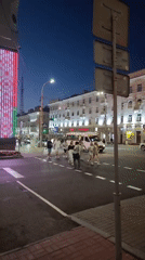Nighttime street crossing near a lit downtown block in Homyel