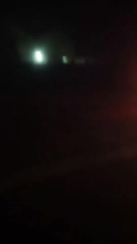 The video shows a night scene with flashing lights, likely from an emergency vehicle. The camera is moving, creating a blurry effect. In the first frame, a red and blue light bar is visible on the right side of the screen, along with headlights in the distance. The second frame focuses on a bright blue light. The third and fourth frames show red taillights and faint lights in the distance respectively. The overall impression is of a moving vehicle with emergency lights activated at night.