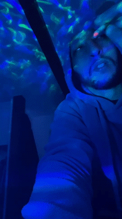 Person in hoodie observed in colorful lit spaces, Bischheim